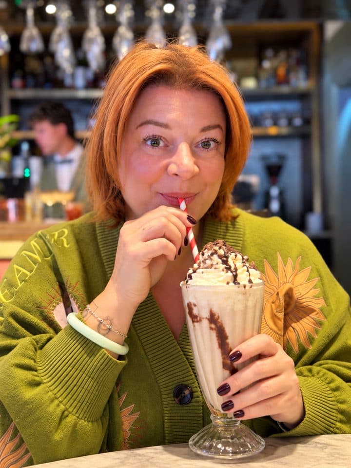 Karen sipping a chocolate milkshake with whipped cream through a striped straw